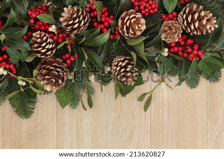 Christmas and winter background border with holly, pine cones, mistletoe and fir background border over oak wood.