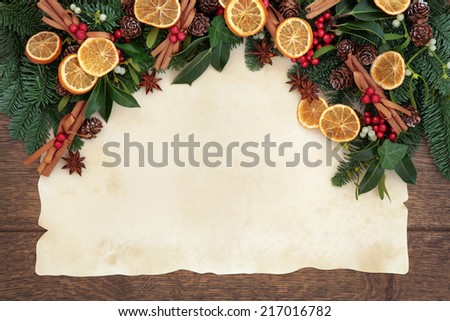 Christmas background border with dried fruit and cinnamon spice with fir, holly, ivy, mistletoe and pine cones over old parchment paper and oak .