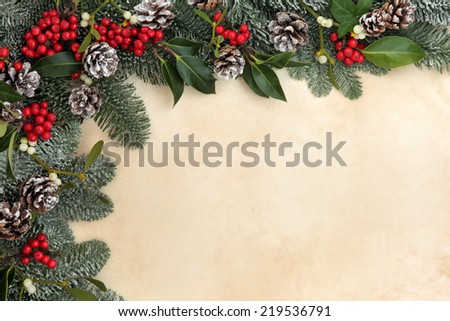 Christmas and winter background border of fir, holly, mistletoe and snow covered pine cones over old parchment.