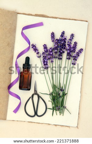 Lavender herb flower stems, aromatherapy bottle, scissors and purple ribbon on a hemp paper notebook over mottled cream background.