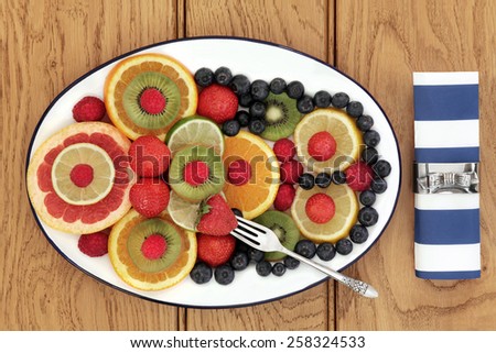 Fruit selection for antioxidant  health food diet on an oval plate with old silver fork and napkin with ring over oak background.