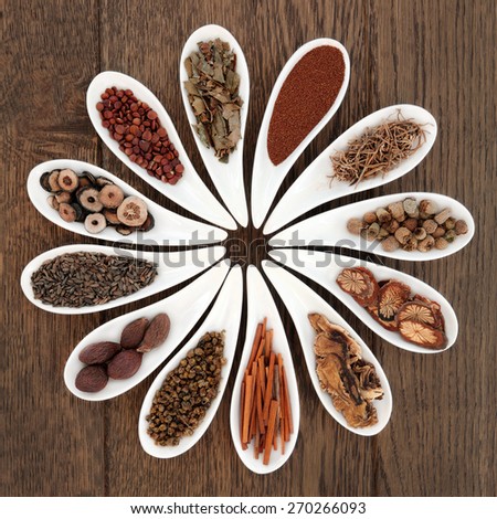 Chinese herbal medicine selection in porcelain dishes over oak background.