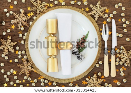 Christmas holiday dinner place setting with plates, napkin, cutlery, gold bauble decorations over oak table background.