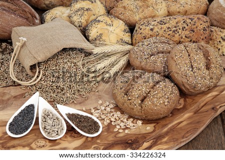 Seeded bread roll selection with wheat sheaths, rye grain in a hessian sack with chia, sunflower and caraway seed on an olive wood board.