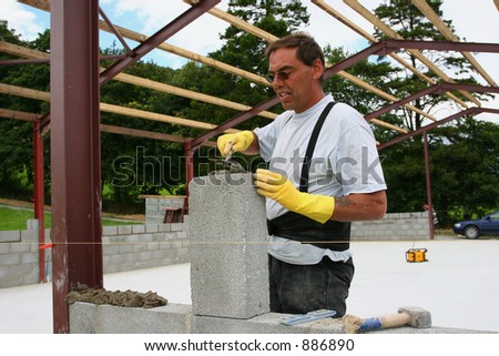 A man trowelling cement onto a concrete block on a building site and wearing rubber gloves to protect his hands.