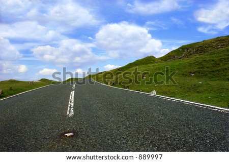 A steep uphill road with grass verges on either side with a blue sky and clouds. Set in the Brecon Beacons National Park, Wales UK