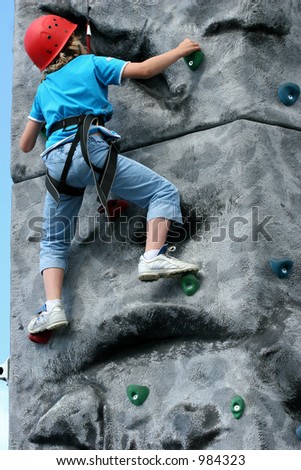 Young girl climbing  on a training rock face, wearing a harness and red hard hat.