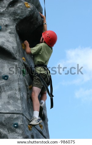 Boy climbing  on a training rock face, wearing a harness and red hard hat.