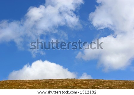 Barren grass hillside against a blue sky with alto cumulus clouds.