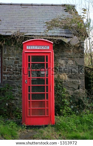 Red British old telephone box next to a derelict wall of an old cottage.