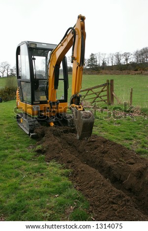 Mini digger standing in a field next to a newly dug trench.