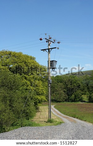 Electricity transformer standing next to a gravel driveway in a rural location.