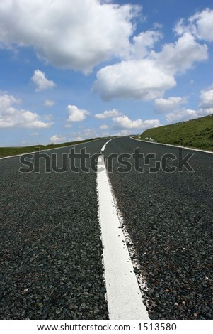 Uphill road featuring the central white line and a blue sky with cumulus clouds.