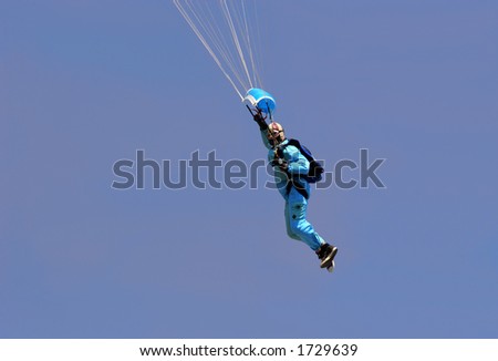 Male parachutist wearing a blue boiler suit, flying against a blue sky.