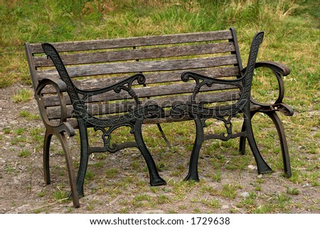 Old wooden and metal bench with spare black metal sides standing on the grass.