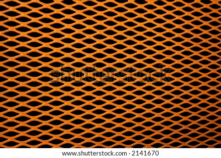 Gold colored metal grill of diamond shaped mesh, against black.