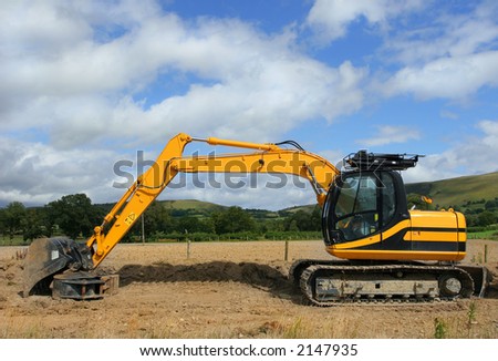 Yellow digger standing idle on a building construction site with rural countryside and a blue sky with clouds to the rear.