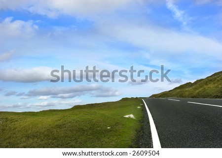 Steep uphill road with grass verges on either side with a blue sky and alto cumulus clouds. set in the Brecon Beacons National Park, Wales, United Kingdom.