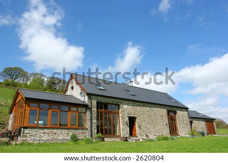 Newly restored residential stone barn with a slate roof in rural countryside against a blue sky with clouds.