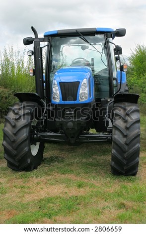 New blue and black four wheel drive tractor standing idle in a field.
