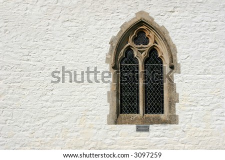 Gothic leaded glass window set within a white washed church stone wall.