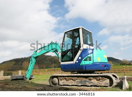 Mini digger standing idle on rough ground in rural countryside.