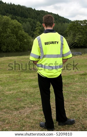 Male security guard standing alone in rural countryside. Rear view.