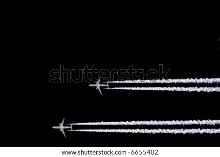Two jet aircraft flying in a horizontal and parallel formation with smoke trails, set against a black sky background.