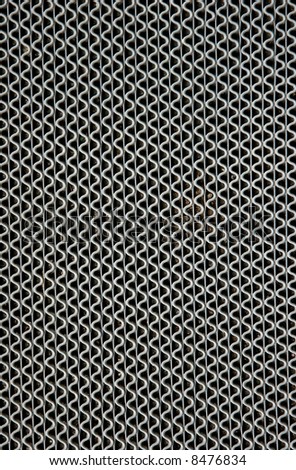 Vertical wavy silver lines of a metal grate on a pathway.