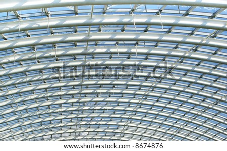 Curved reinforced steel roof joists in a conservatory roof, with glass panes in between and blue sky beyond.