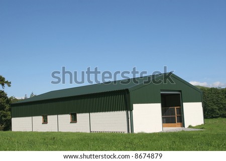 Newly constructed barn of cream painted concrete block walls with a green metal sheet roof,set against a blue sky and trees to the rear.