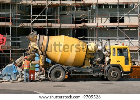 Yellow cement mixer truck in front of a building under construction, faced with scaffolding.