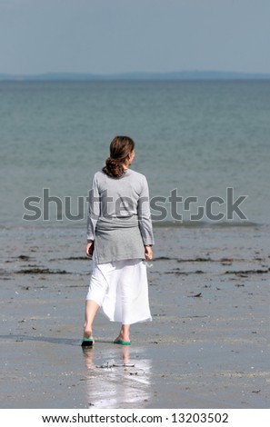 Female standing on a beach in summer gazing out to sea. Rear View.