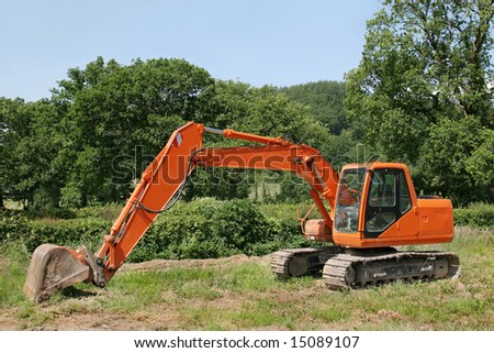 Orange digger standing idle in a field with trees and a blue sky to the rear.