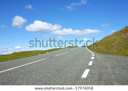 Uphill road in rural countryside with grass verges either  side, set against a blue sky with clouds. Set in the Brecon Beacons National Park, Wales, United Kingdom.