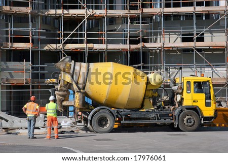 Cement mixer truck parked in front of a new building under construction with scaffolding.
