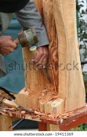 Hands of an elderly man, carving a wood sculpture with a chisel and mallet.