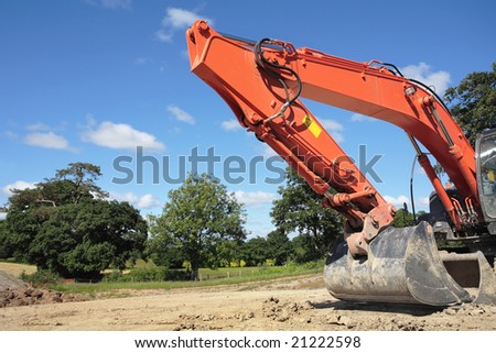 Industrial orange digger bucket with hydraulics standing idle in rural countryside, against a blue sky and clouds.