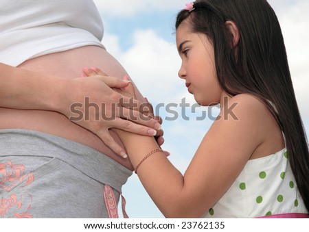 Young girl touching the belly and hands of her pregnant mother.