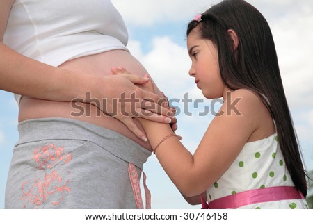 Young girl touching the belly and hands of her pregnant mother.