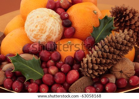 Cranberry and orange fruit with mixed nuts, and holly leaf sprigs and pine cones, isolated over white background.