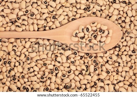 Black eyed peas in a wooden spoon and forming a background.