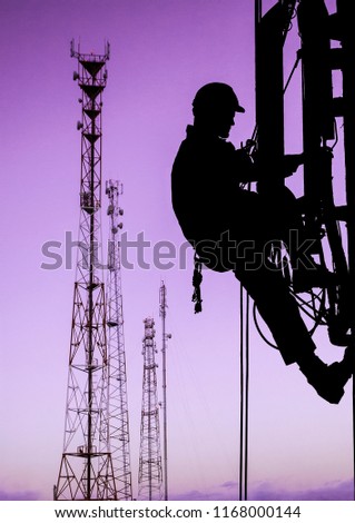 Silhouette of professional industrial climber in helmet and uniform works at height for instaling communication equipment and antenna and telecommunication towers with sunset sky as background. Risky