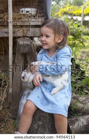 Sweet little girl 3 years old hugs her baby rabbit in the farm yard