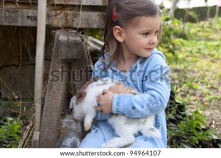Sweet little girl 3 years old hugs her baby rabbit in the farm yard