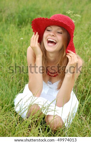 Beautiful teenage girl smiling from ear to ear wearing a red hat and sitting on meadow.