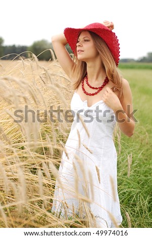 Teenage girl standing next to a rye field wearing a red hat and looking to the side