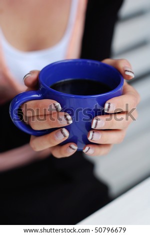 Woman\'s hands holding a blue cup of coffee; small depth of field