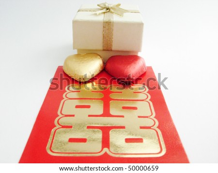A white gift or jewelry box with two heart shape candy and a Chinese double happiness red packet.