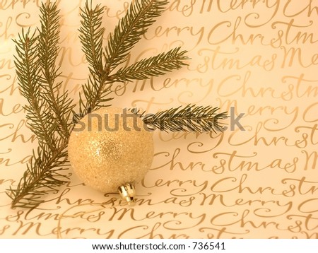 Gold Christmas decorative ball with  evergreen sprig on 'Merry Christmas' writing background